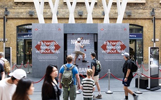 Actor climbing a 3.5-metre rotating climbing wall, symbolizing the struggle people who suffer from homelessness endure (22 June at London’s Kings Cross Station)